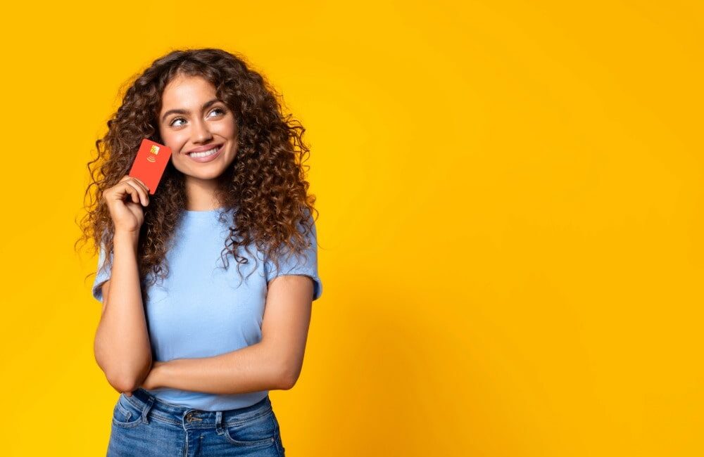 Mujer joven sostiene una tarjeta sobre fondo amarillo, pensando en solicitar un microcrédito en línea