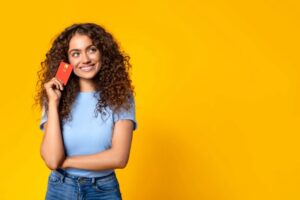 Mujer joven sostiene una tarjeta sobre fondo amarillo, pensando en solicitar un microcrédito en línea