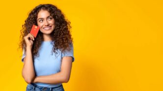 Mujer joven sostiene una tarjeta sobre fondo amarillo, pensando en solicitar un microcrédito en línea